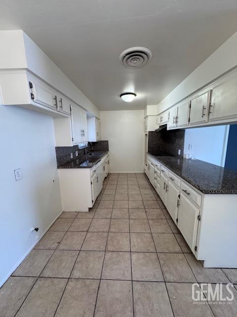 kitchen with white cabinetry, backsplash, light tile patterned floors, and dark stone counters