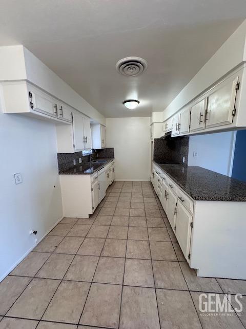 kitchen featuring sink, white cabinets, backsplash, dark stone counters, and light tile patterned floors