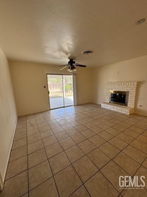 unfurnished living room featuring ceiling fan, a brick fireplace, and light tile patterned floors