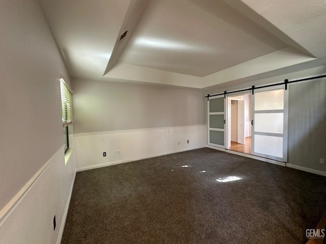 empty room featuring dark carpet, a barn door, and a raised ceiling