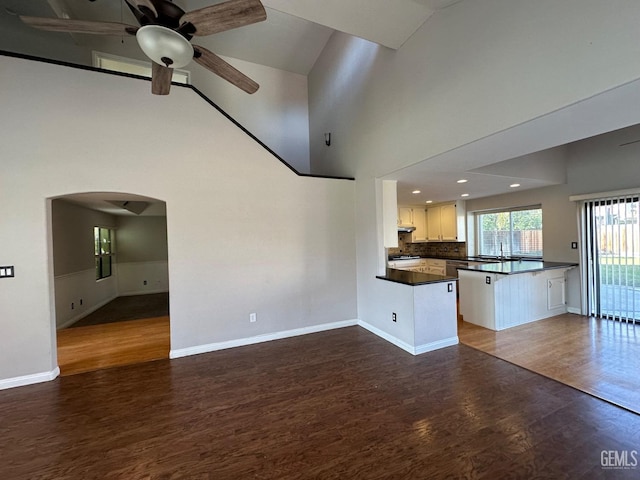 unfurnished living room with ceiling fan, sink, high vaulted ceiling, and dark wood-type flooring