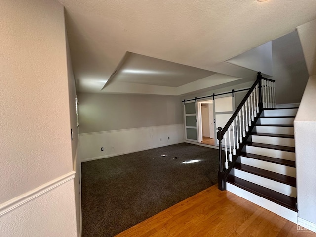 interior space with a raised ceiling, a barn door, and hardwood / wood-style flooring