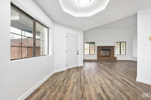 unfurnished living room with baseboards, lofted ceiling, a brick fireplace, and wood finished floors