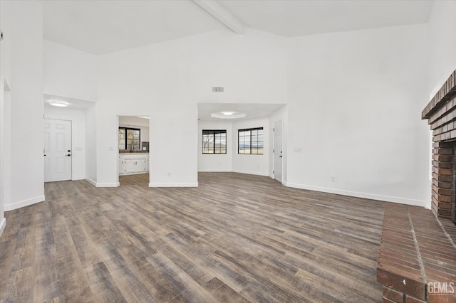 unfurnished living room with a brick fireplace, baseboards, beam ceiling, wood finished floors, and high vaulted ceiling