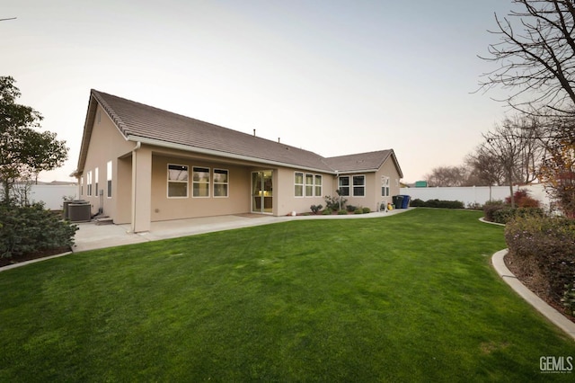 back house at dusk with a yard, a patio, and central AC