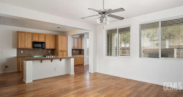 5400 Saddleback Ridge Ct, Bakersfield, CA 93313 - kitchen featuring black microwave, decorative backsplash, ceiling fan, a breakfast bar area, and wood finished floors