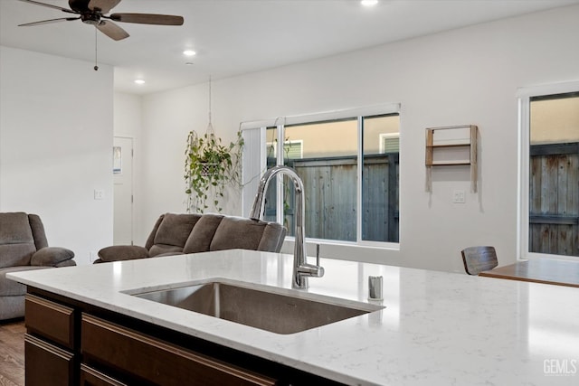 kitchen with dark brown cabinetry, ceiling fan, open floor plan, and a sink