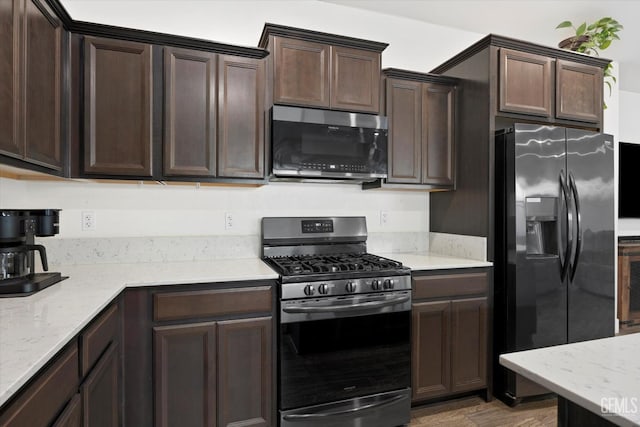 kitchen with dark brown cabinetry, stainless steel appliances, wood finished floors, and light stone countertops
