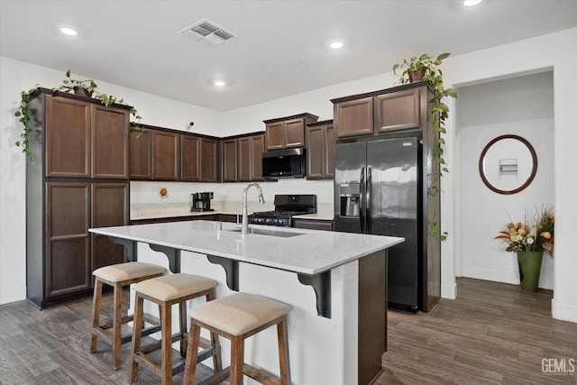 kitchen featuring a sink, visible vents, gas range oven, dark brown cabinetry, and refrigerator with ice dispenser