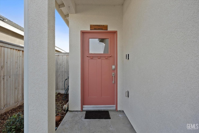 view of exterior entry featuring stucco siding and fence