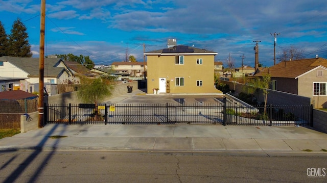 view of front facade featuring a fenced front yard, roof mounted solar panels, stucco siding, and a gate