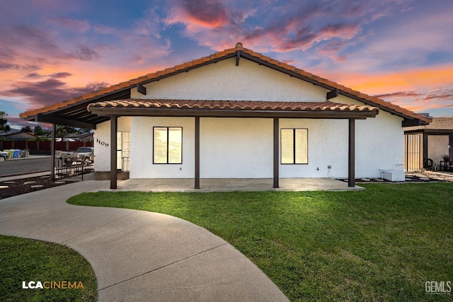 1109 Bell Ave, Taft, CA 93268 - back of house at dusk with a yard, stucco siding, a tiled roof, and a patio area