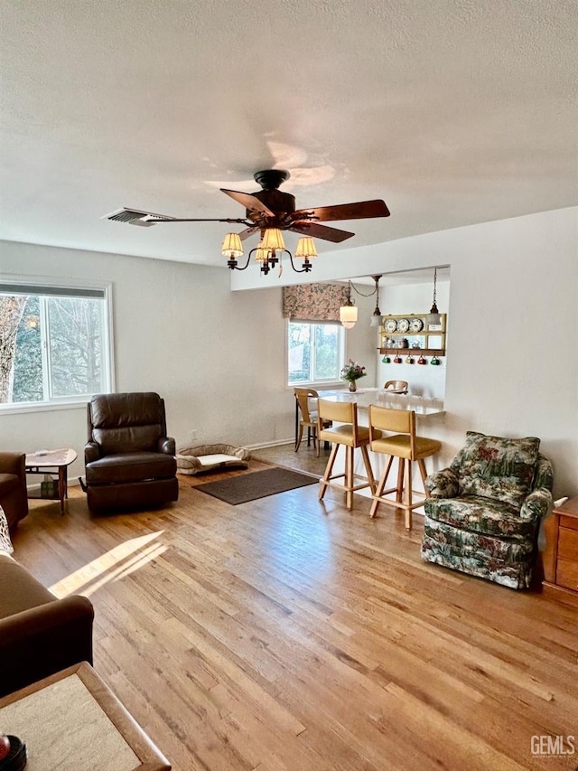 living room with light wood-type flooring, ceiling fan, and a textured ceiling