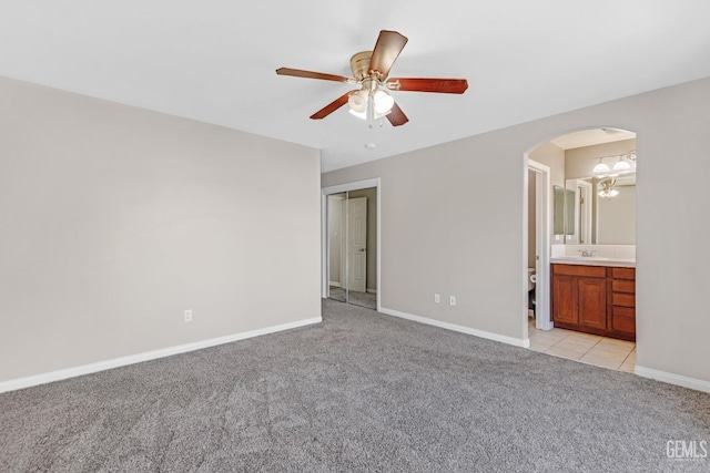 unfurnished bedroom featuring light carpet, ceiling fan, sink, connected bathroom, and a closet