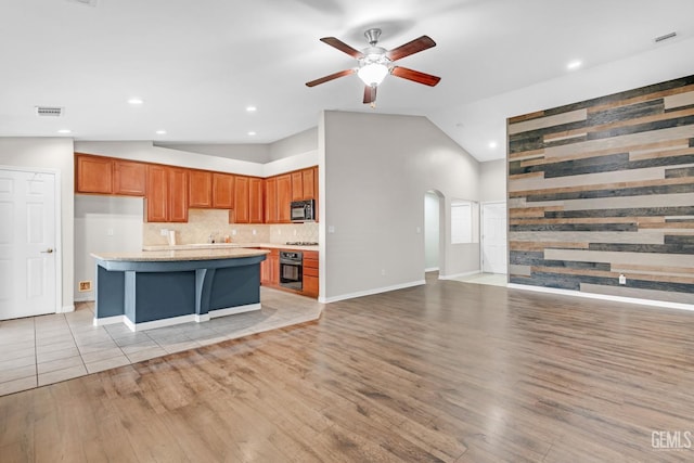 kitchen with vaulted ceiling, ceiling fan, a kitchen island, light hardwood / wood-style floors, and oven