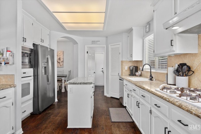 5812 Seasons Valley Ct, Bakersfield, CA 93313 - kitchen with appliances with stainless steel finishes, under cabinet range hood, arched walkways, white cabinetry, and dark wood-style flooring