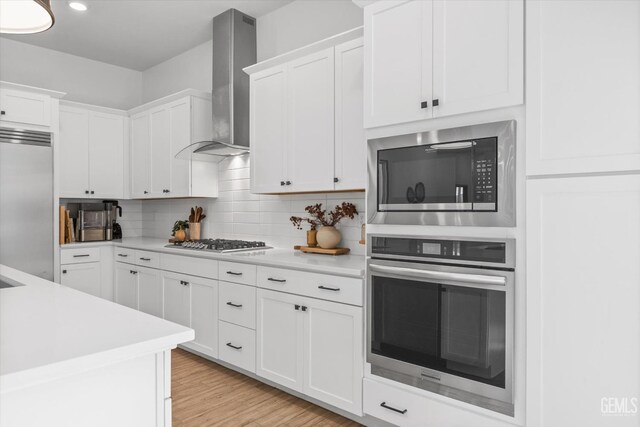 kitchen with decorative backsplash, built in appliances, white cabinetry, and wall chimney exhaust hood