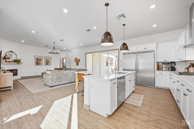 kitchen featuring white cabinets, pendant lighting, stainless steel appliances, and a kitchen island with sink