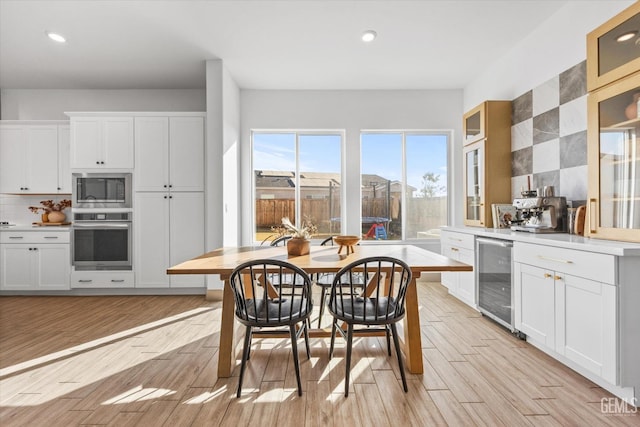 kitchen featuring white cabinets, oven, built in microwave, light hardwood / wood-style floors, and beverage cooler