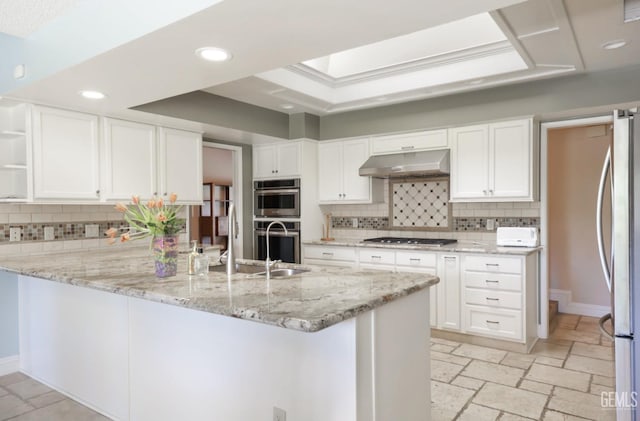 kitchen featuring under cabinet range hood, a peninsula, stone tile flooring, stainless steel appliances, and a raised ceiling