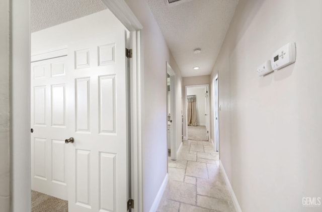 hallway featuring stone tile floors, a textured ceiling, and baseboards