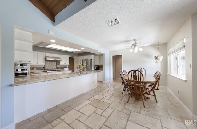 unfurnished dining area with baseboards, visible vents, ceiling fan, stone tile flooring, and a textured ceiling