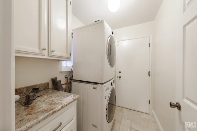 laundry room with cabinet space, stacked washer and clothes dryer, and baseboards