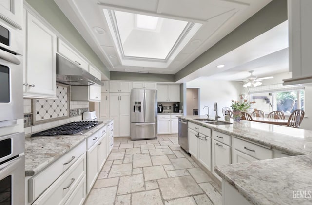 kitchen featuring under cabinet range hood, stone tile floors, appliances with stainless steel finishes, white cabinets, and a sink