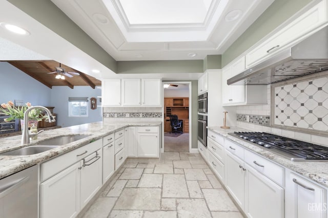 kitchen with a sink, stone tile floors, appliances with stainless steel finishes, white cabinets, and a raised ceiling