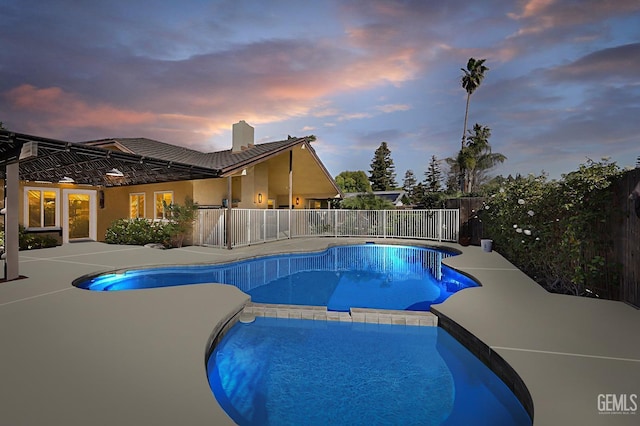 pool at dusk featuring a patio area, fence, and a pool with connected hot tub