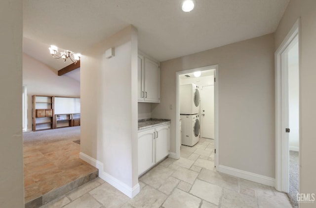 corridor featuring stone tile floors, baseboards, a chandelier, and stacked washing maching and dryer