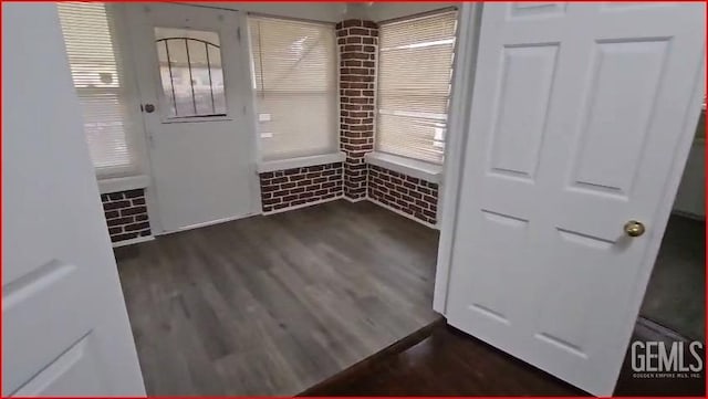 interior space with dark wood-type flooring and brick wall