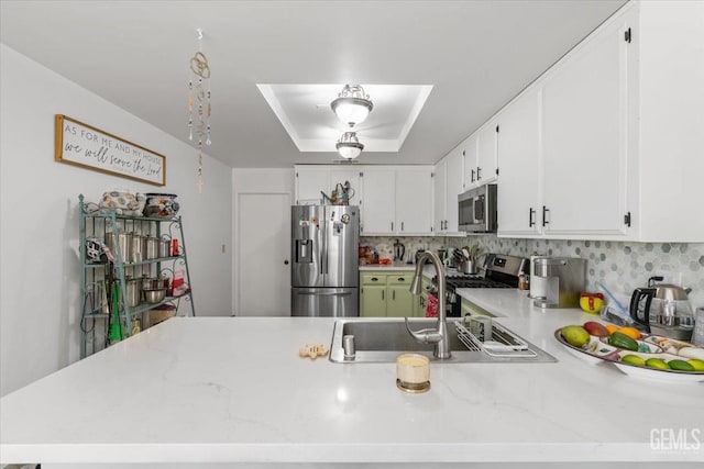 kitchen featuring a peninsula, a sink, appliances with stainless steel finishes, backsplash, and a raised ceiling