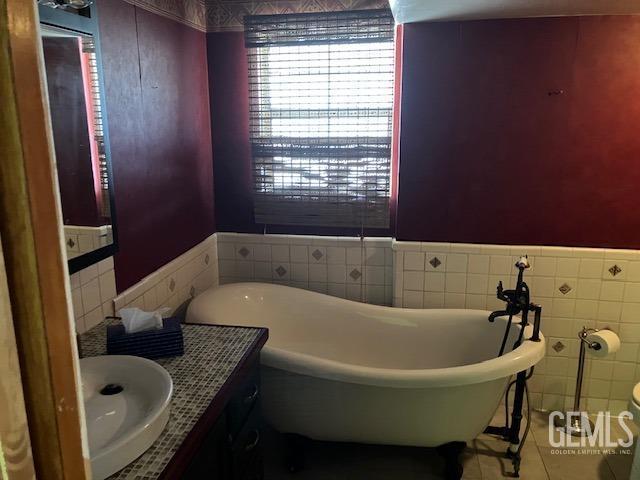 6419 Ringsdale Ct, Bakersfield, CA 93313 - bathroom featuring vanity, a freestanding tub, tile patterned floors, a wainscoted wall, and tile walls