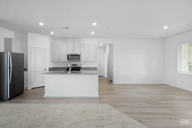 kitchen featuring light stone counters, visible vents, white cabinetry, appliances with stainless steel finishes, and a center island with sink