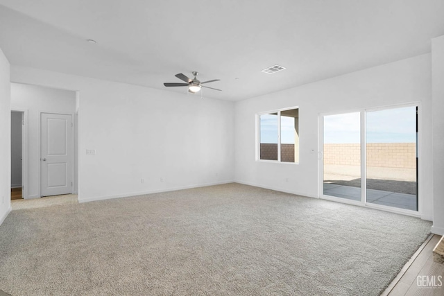 spare room with light colored carpet, visible vents, ceiling fan, and baseboards