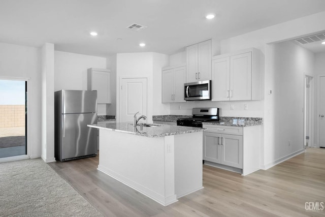 kitchen with light wood finished floors, stainless steel appliances, white cabinets, a kitchen island with sink, and a sink