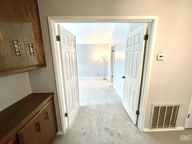 hallway with baseboards, visible vents, and light colored carpet