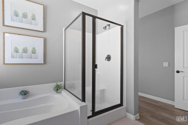 bathroom with a stall shower, baseboards, a bath, and wood finished floors