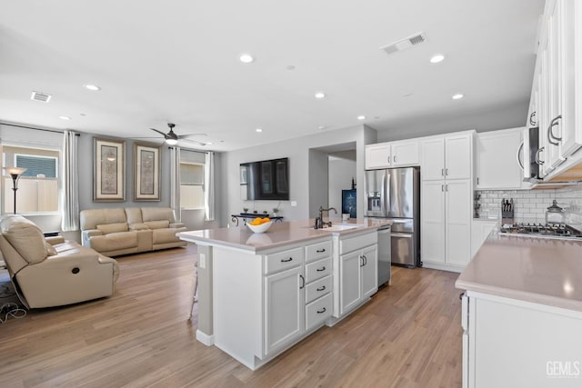 kitchen with open floor plan, visible vents, a kitchen island with sink, and white cabinetry