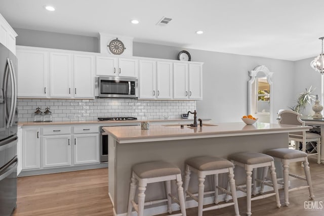 kitchen with appliances with stainless steel finishes, light countertops, hanging light fixtures, and white cabinetry