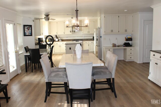 dining space featuring ceiling fan with notable chandelier, ornamental molding, and dark wood-type flooring