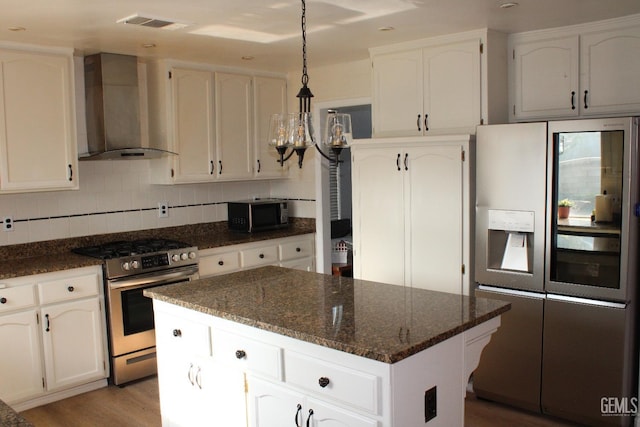 kitchen with hanging light fixtures, wall chimney range hood, a kitchen island, white cabinets, and appliances with stainless steel finishes