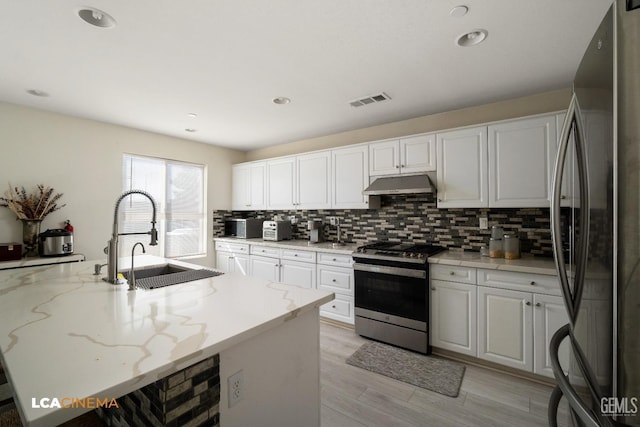 kitchen featuring sink, white cabinets, a kitchen island with sink, stainless steel appliances, and light stone countertops