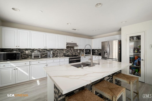 kitchen featuring stainless steel appliances, an island with sink, sink, and white cabinetry