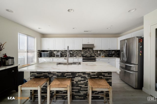 kitchen with backsplash, white cabinets, a kitchen breakfast bar, a kitchen island with sink, and stainless steel appliances