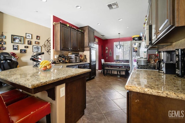 kitchen with light stone countertops, a kitchen bar, kitchen peninsula, and decorative light fixtures