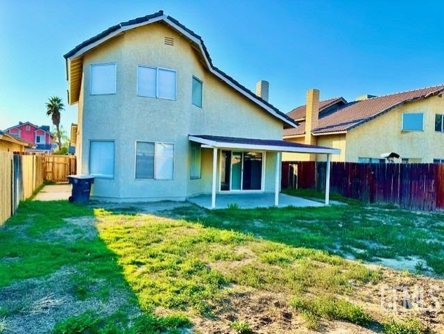 rear view of property with a lawn, a patio area, a fenced backyard, and stucco siding