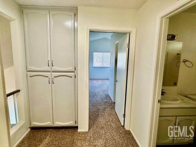 hallway with baseboards, dark colored carpet, and a sink