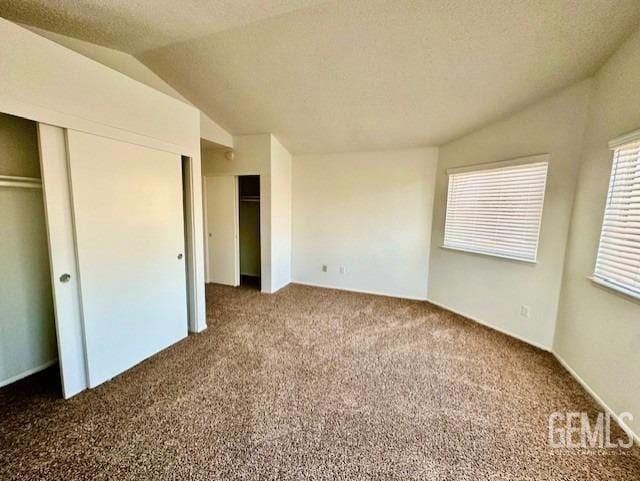 unfurnished bedroom featuring vaulted ceiling, carpet floors, and a textured ceiling